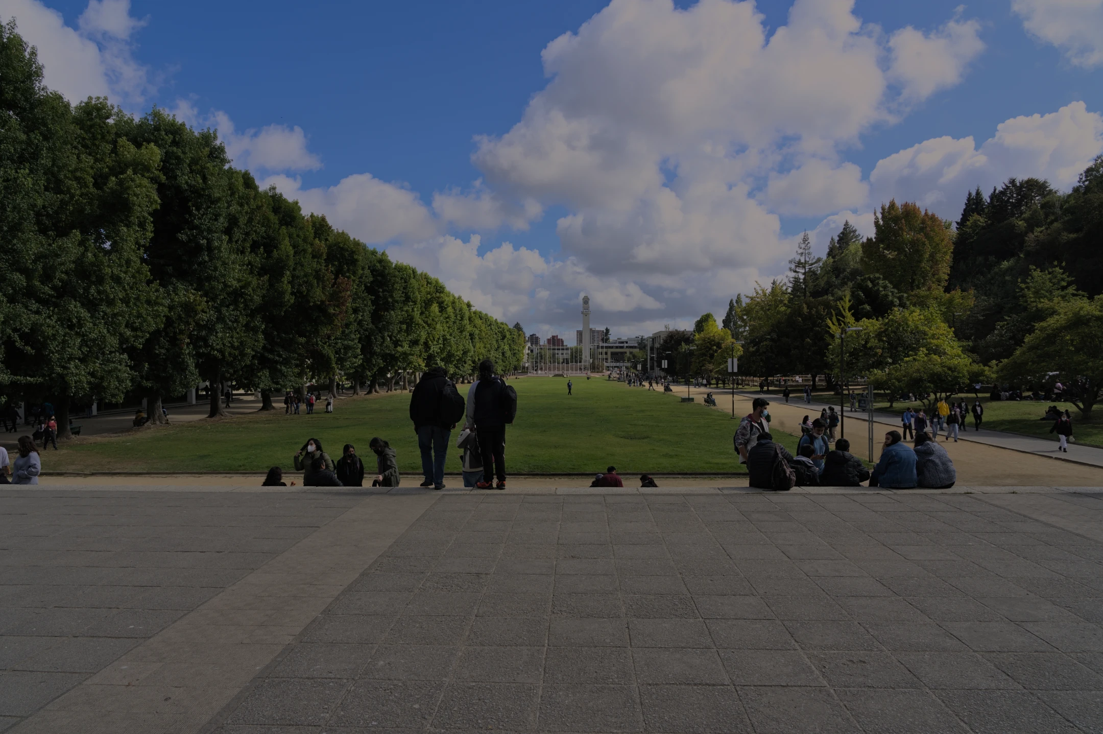 Vista frontal del Foro UdeC: césped central, estudiantes reunidos y edificios al fondo.