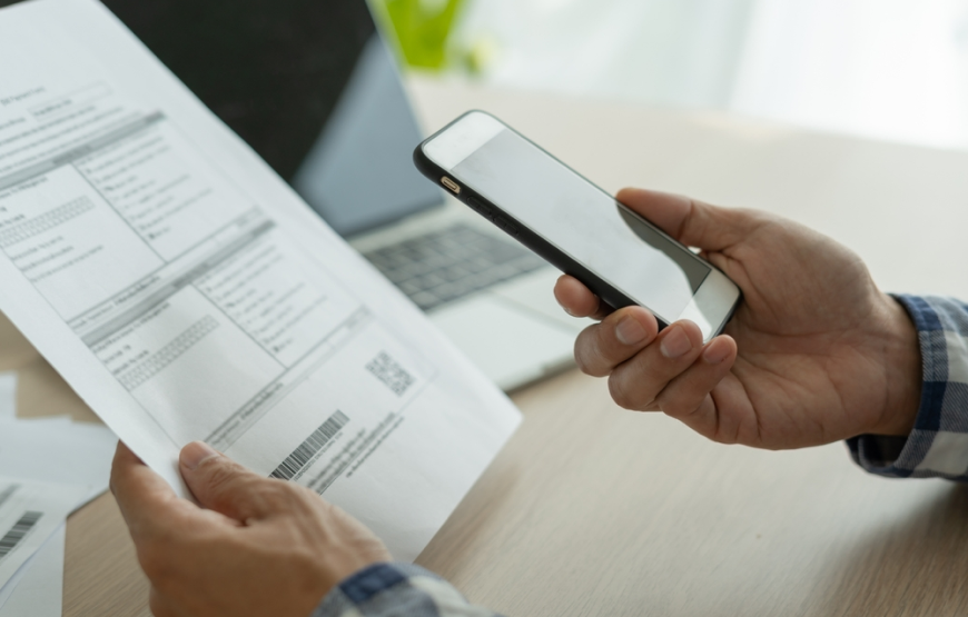 Persona afirma un papel con la mano mientras lo revisa con el celular