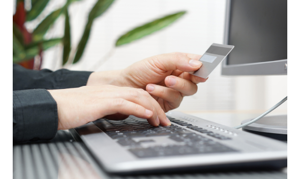 Manos introducen datos en teclado mientras sujetan tarjeta bancaria delante de monitor.